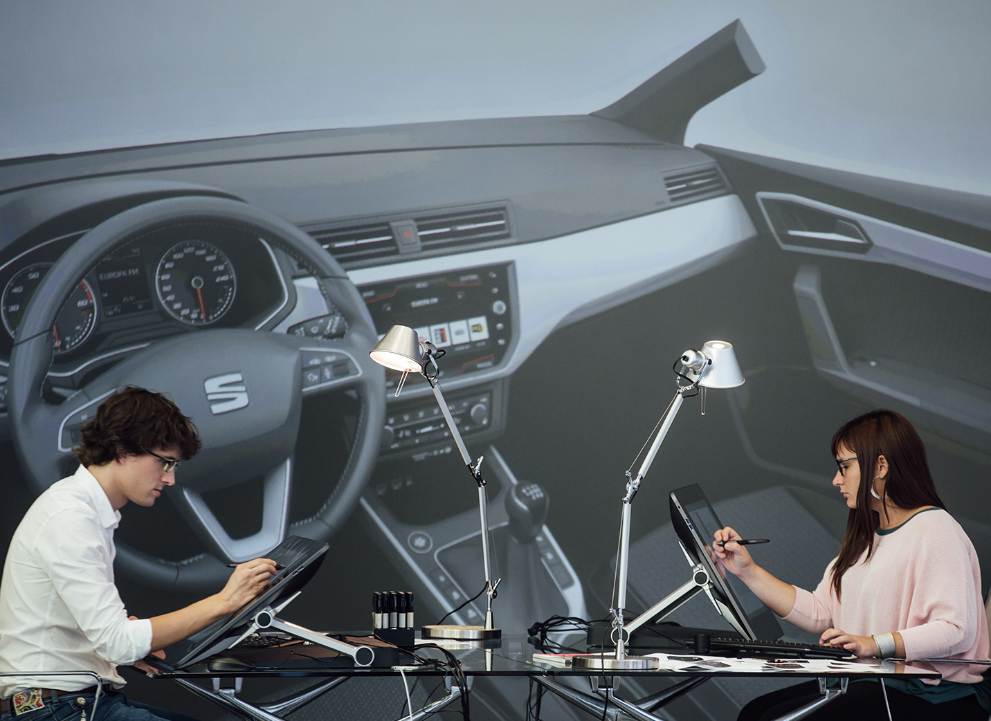 Dos nuevos diseñadores de automóviles dibujan en unidades de visualización electrónicas con un fondo fotográfico del interior de un automóvil - SEAT Recuerso Humanos